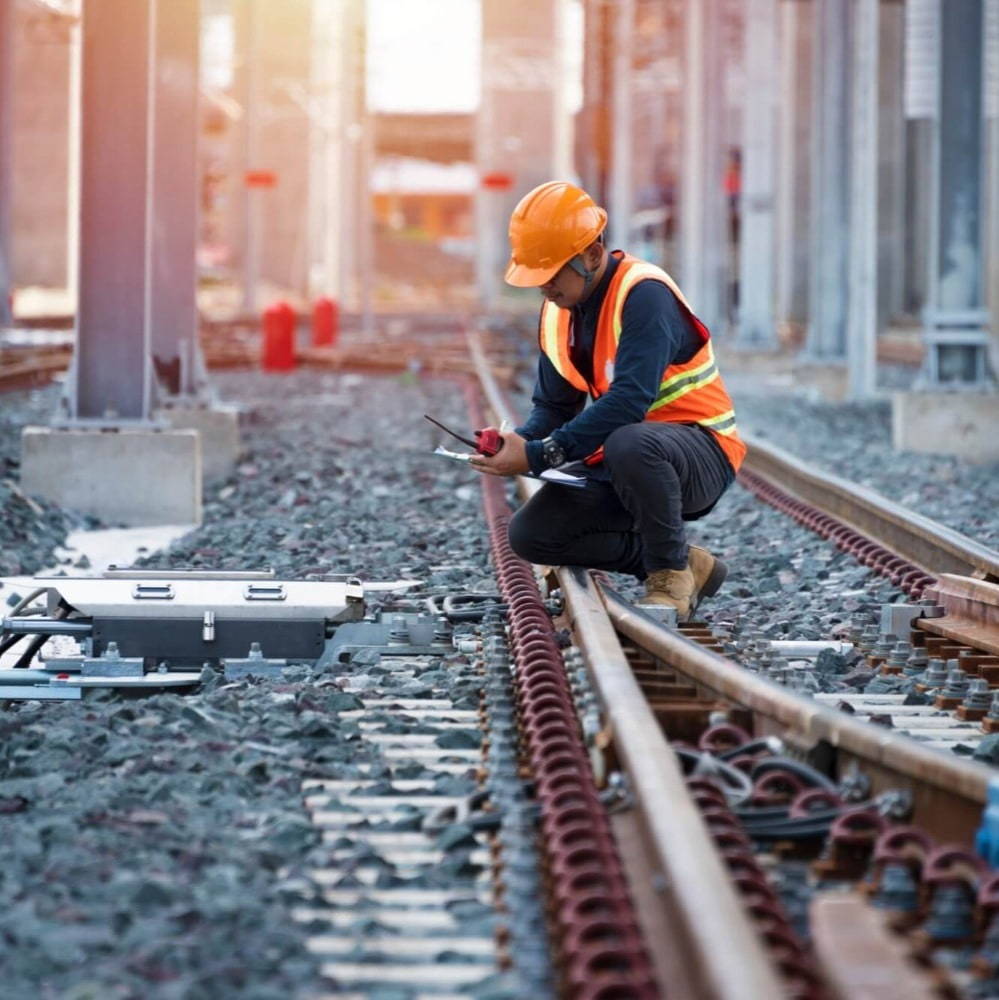 person crouching down on a railway line wearing PPE holding a walkie talkie