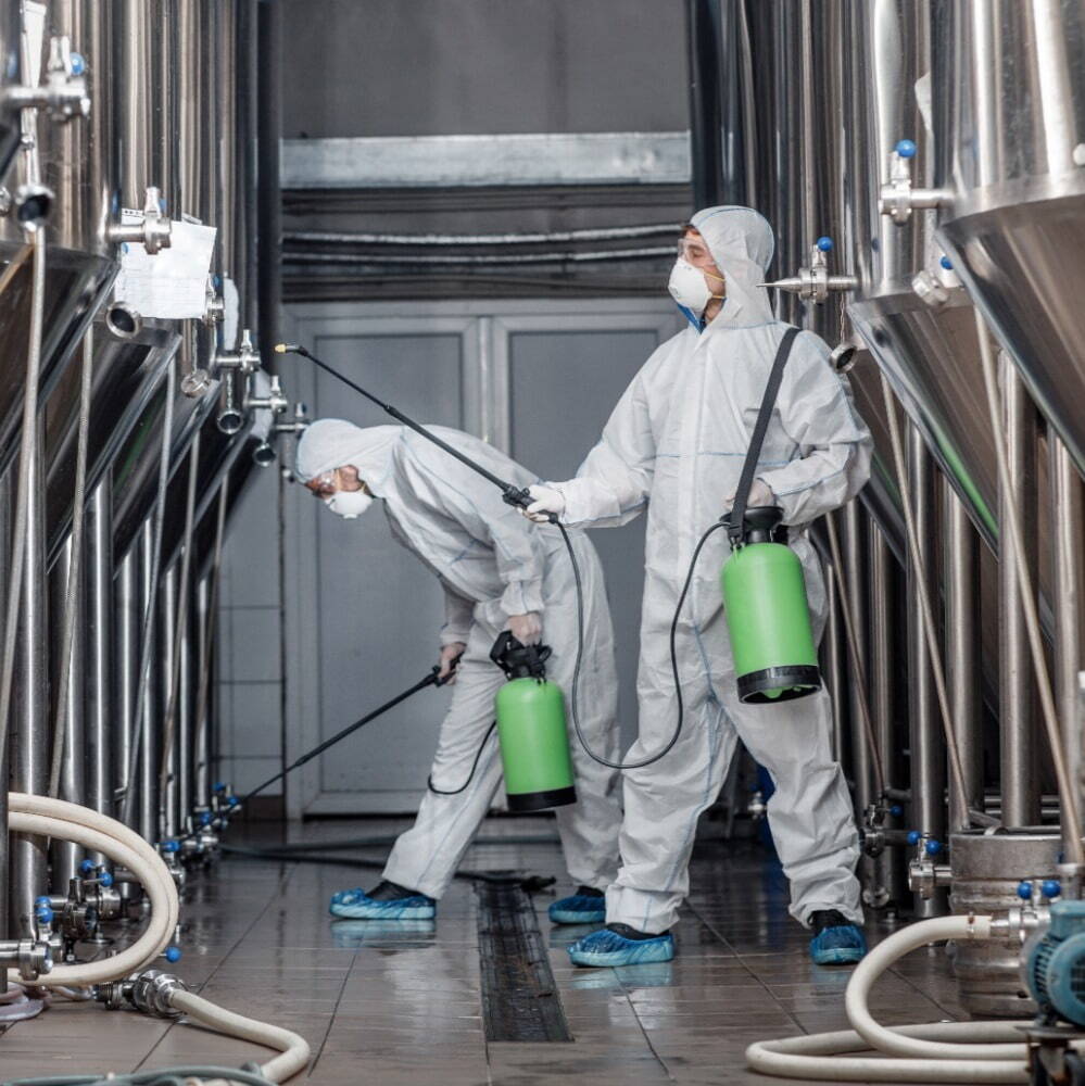 2 people wearing white overalls, face masks and safety glasses doing equipment maintenance 