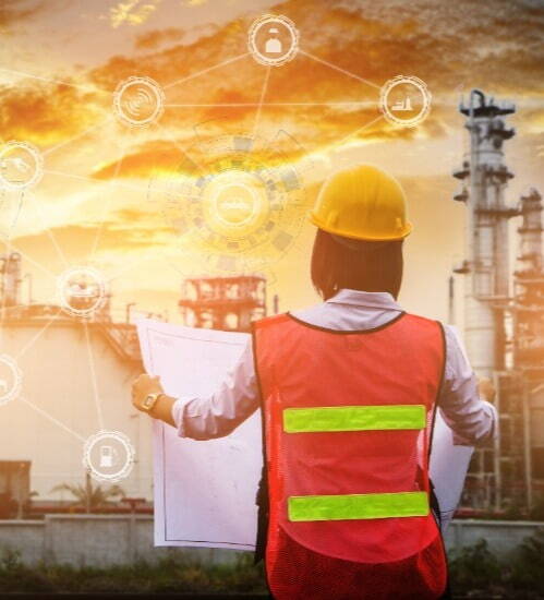 The back of a woman wearing a yellow hard hat and safety vest looking at a large paper document 