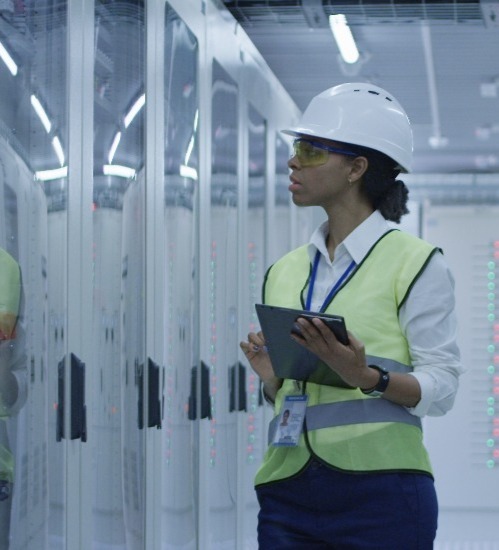 woman wearing white hard hat and yellow safety vest and glasses looking at equipment