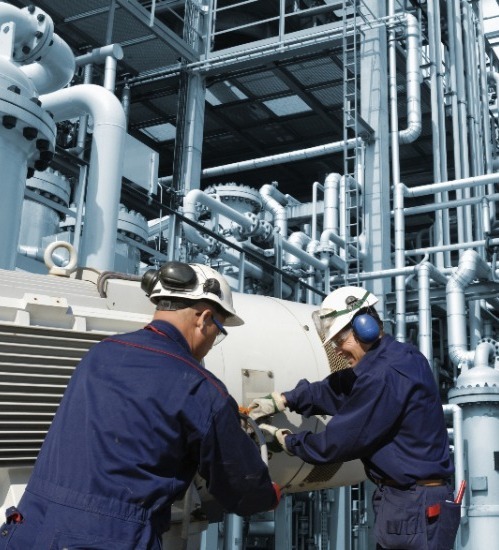 2 men working on equipment wearing blue overalls and white hard hats