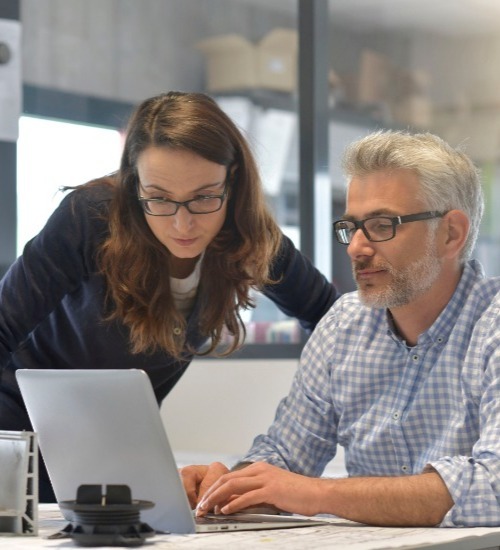 a man and woman stood looking at a laptop on a desk