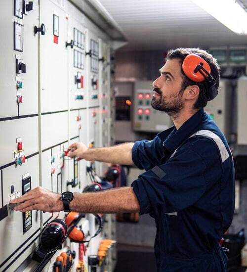 Man looking at equipment wearing blue overalls and orange ear defenders