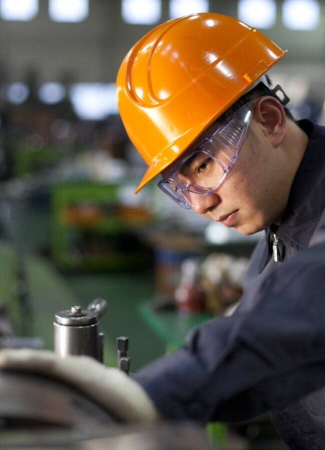 man wearing orange hard hat and safety spectacles looking at equipment 