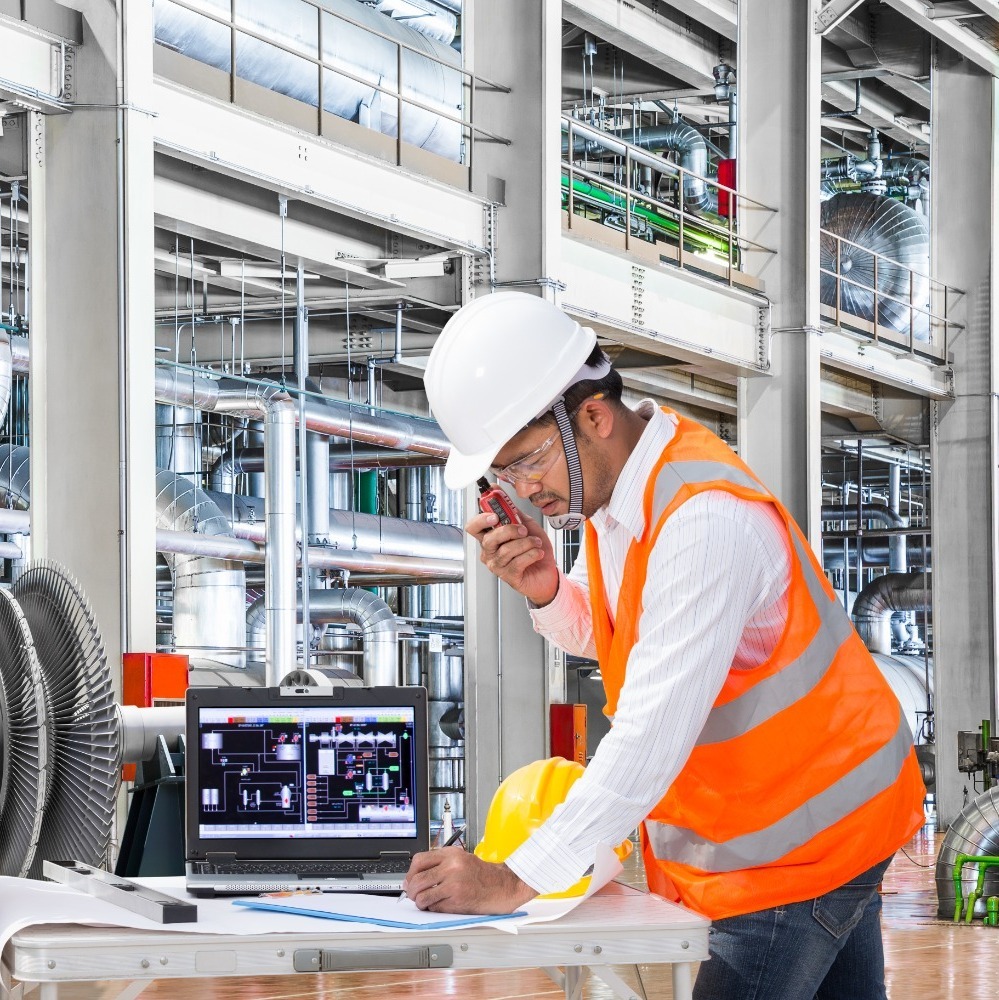 Engineer communicating with colleagues wearing a white hard hat and orange safety vest