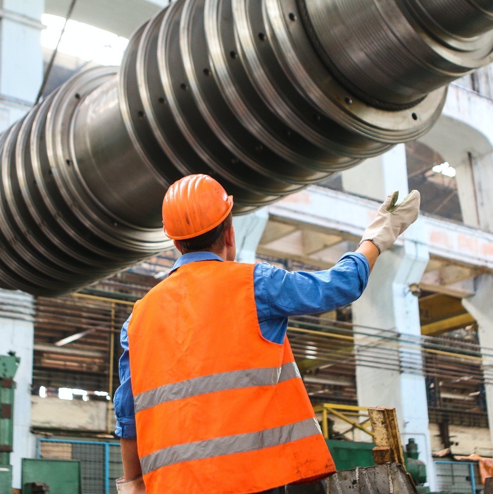 Man in an orange hard hat and safety vest stood under equipment.