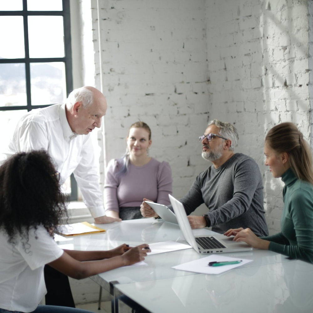 5 people round a table with laptops in a meeting