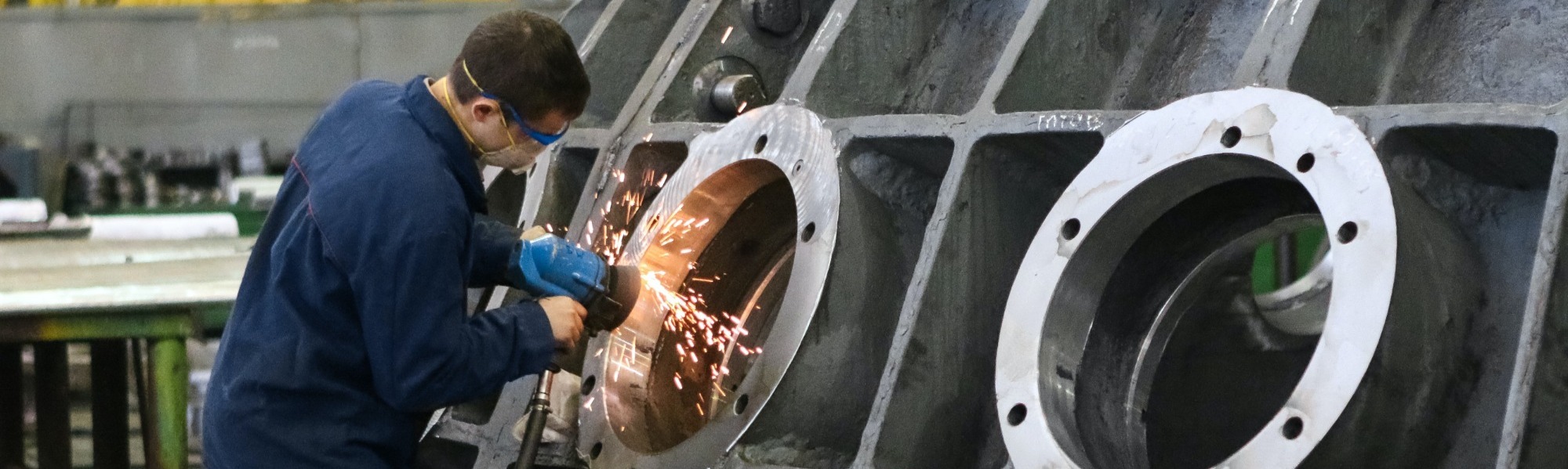 man wearing PPE using an angle grinder on a very large piece of equipment