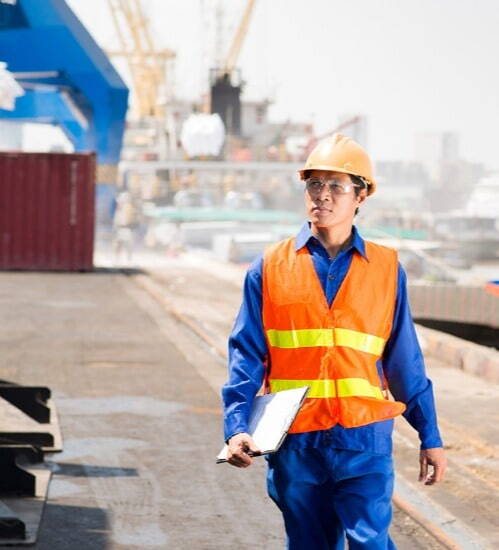 Man wearing yellow hard had and safety gear holding a clipboard