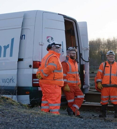 Picture of NRL rail workers outside a white NRL van in orange PPE and hard hats 